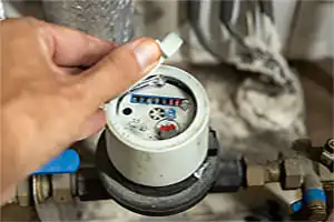 Compteur d'eau, une main ouvre le couvercle pour voir les chiffres d'indiqués
